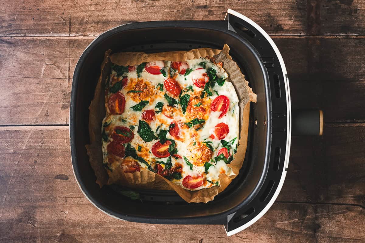 Cooked air fryer frittata inside the basket, golden and puffed with melted cheese and vegetables.
