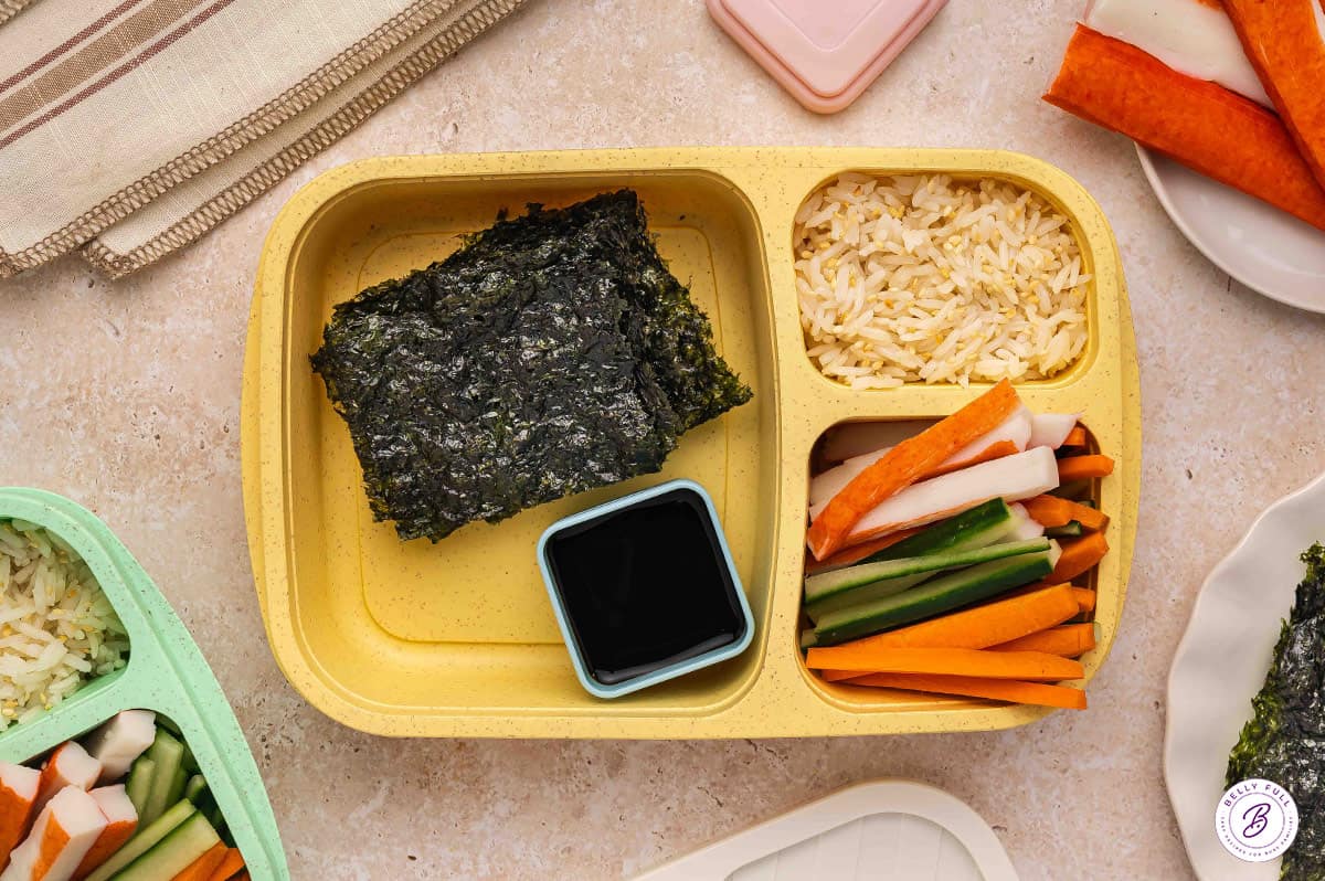 Build your own sushi bento box with roasted seaweed, rice, imitation crab, sliced carrots, sliced cucumber, and soy sauce