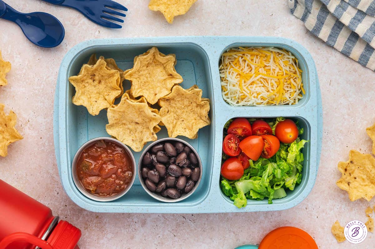 Build your own Taco bento box with tortilla Scoops, black beans, shredded cheese, diced tomatoes, and chopped lettuce
