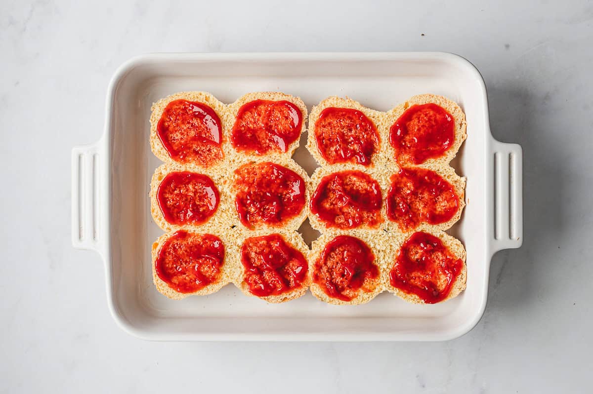 sliced bun bottoms with ketchup spread in casserole dish