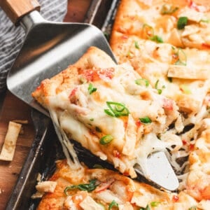 Crispy sheet pan crab rangoon pizza slice lifted from the pan, topped with melty cheese, crab, scallions, and sweet chili drizzle.