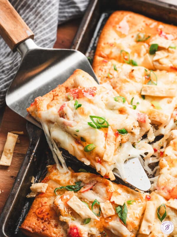 Crispy sheet pan crab rangoon pizza slice lifted from the pan, topped with melty cheese, crab, scallions, and sweet chili drizzle.
