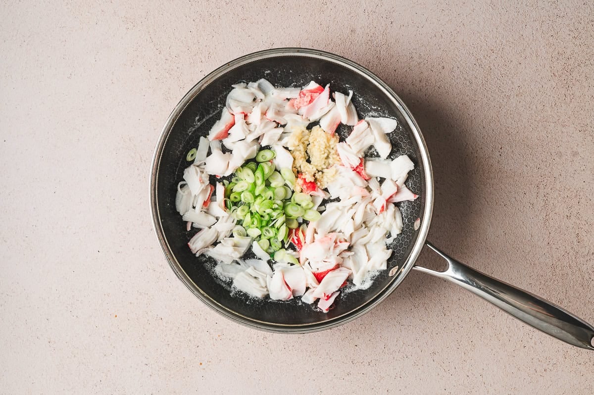 Skillet with crab meat, sliced green onions, and garlic cooking together.