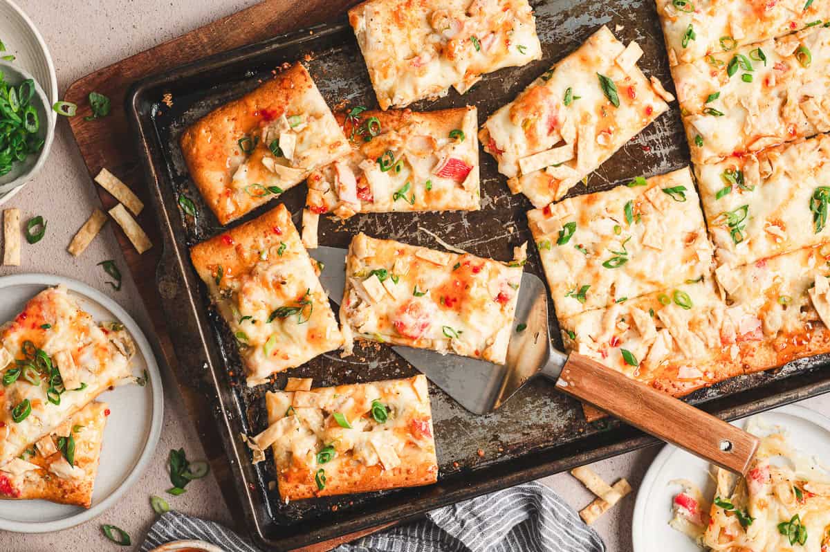 Crab rangoon pizza cut into squares on a sheet pan, topped with scallions and crispy wonton strips.