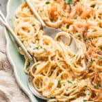 Close-up of creamy caramelized onion pasta on a green serving platter, garnished with fresh parsley and black pepper, with a spoon and fork ready for serving.