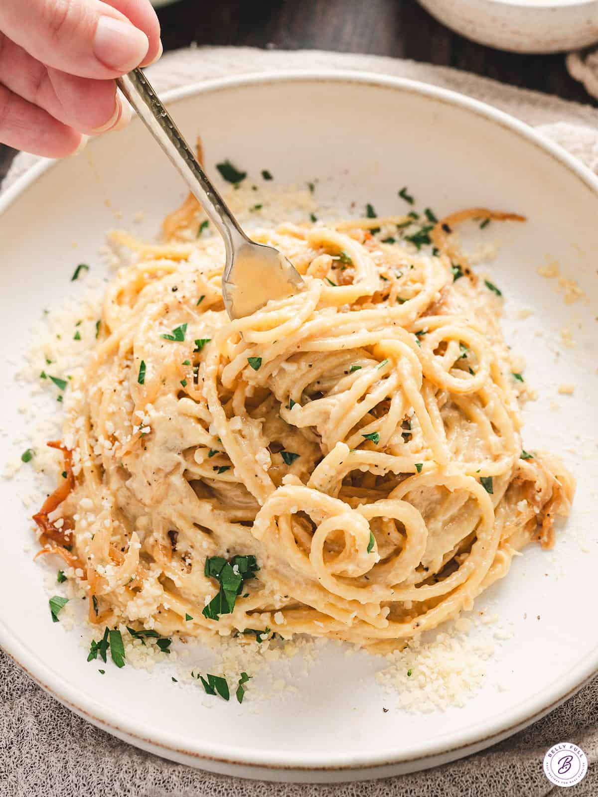 Close-up of creamy caramelized onion pasta on a green serving platter, garnished with fresh parsley and black pepper, with a spoon and fork ready for serving.