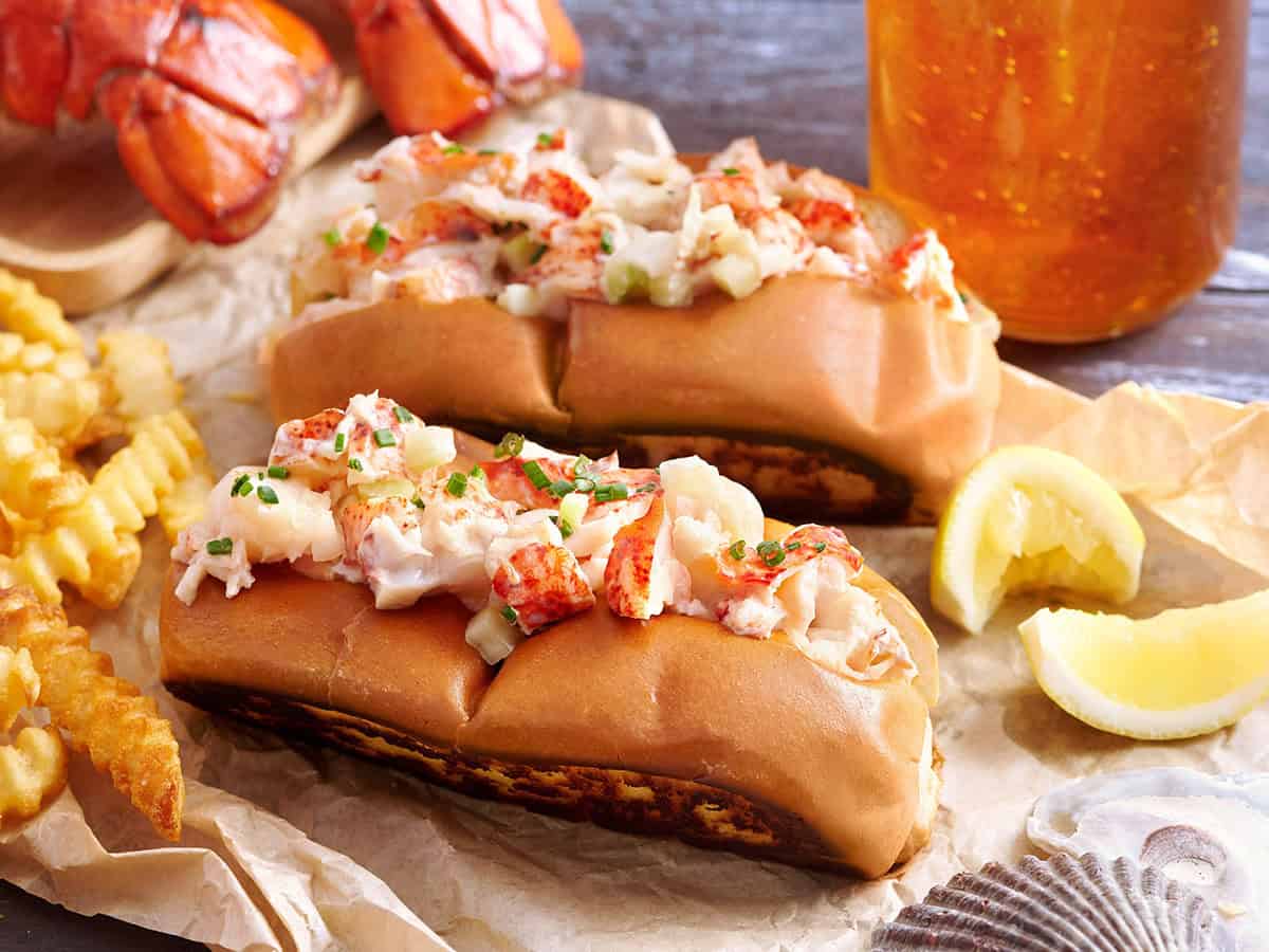 Close-up of lobster rolls with potato chips, lobster tails, and beer on the side.