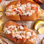 Close-up of two buttery toasted buns filled with lobster salad and garnished with fresh herbs.