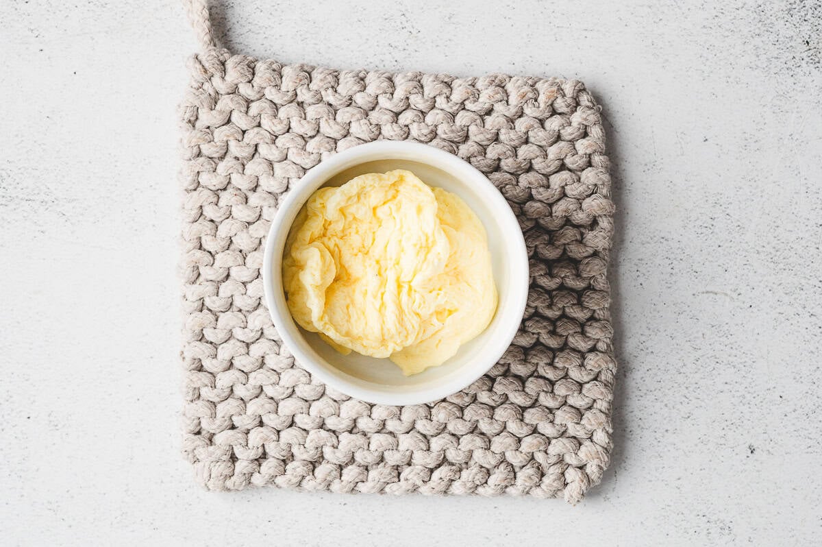 Freshly microwaved soufflé-style egg puffed up inside a white ramekin set on a textured potholder.