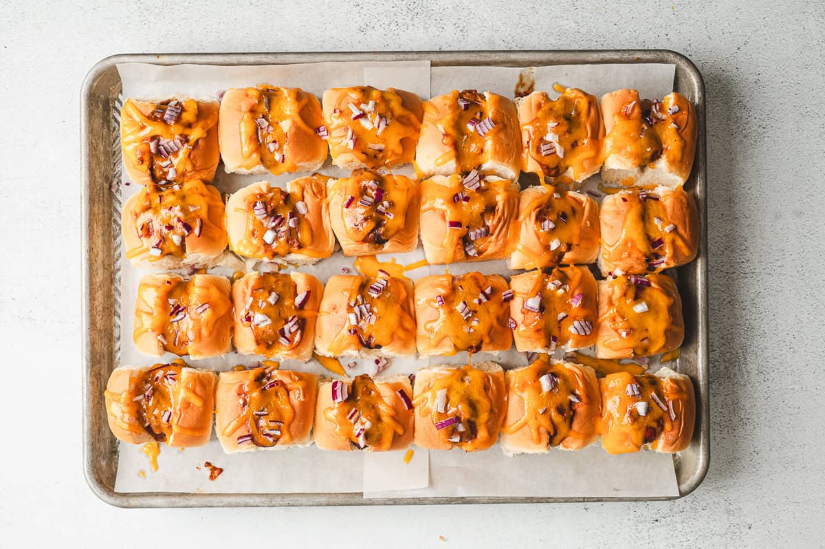 Mini chili cheese dogs fresh from the oven with melted cheddar and red onion on top.