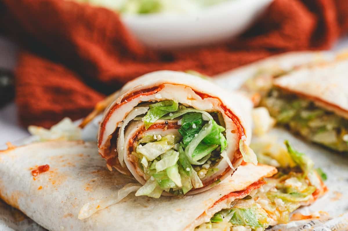 Rolled pizza salad wrap sliced to show layers of melted cheese, pepperoni, and lettuce filling.