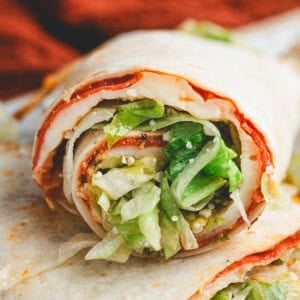 Rolled pizza salad wrap sliced to show layers of melted cheese, pepperoni, and lettuce filling.