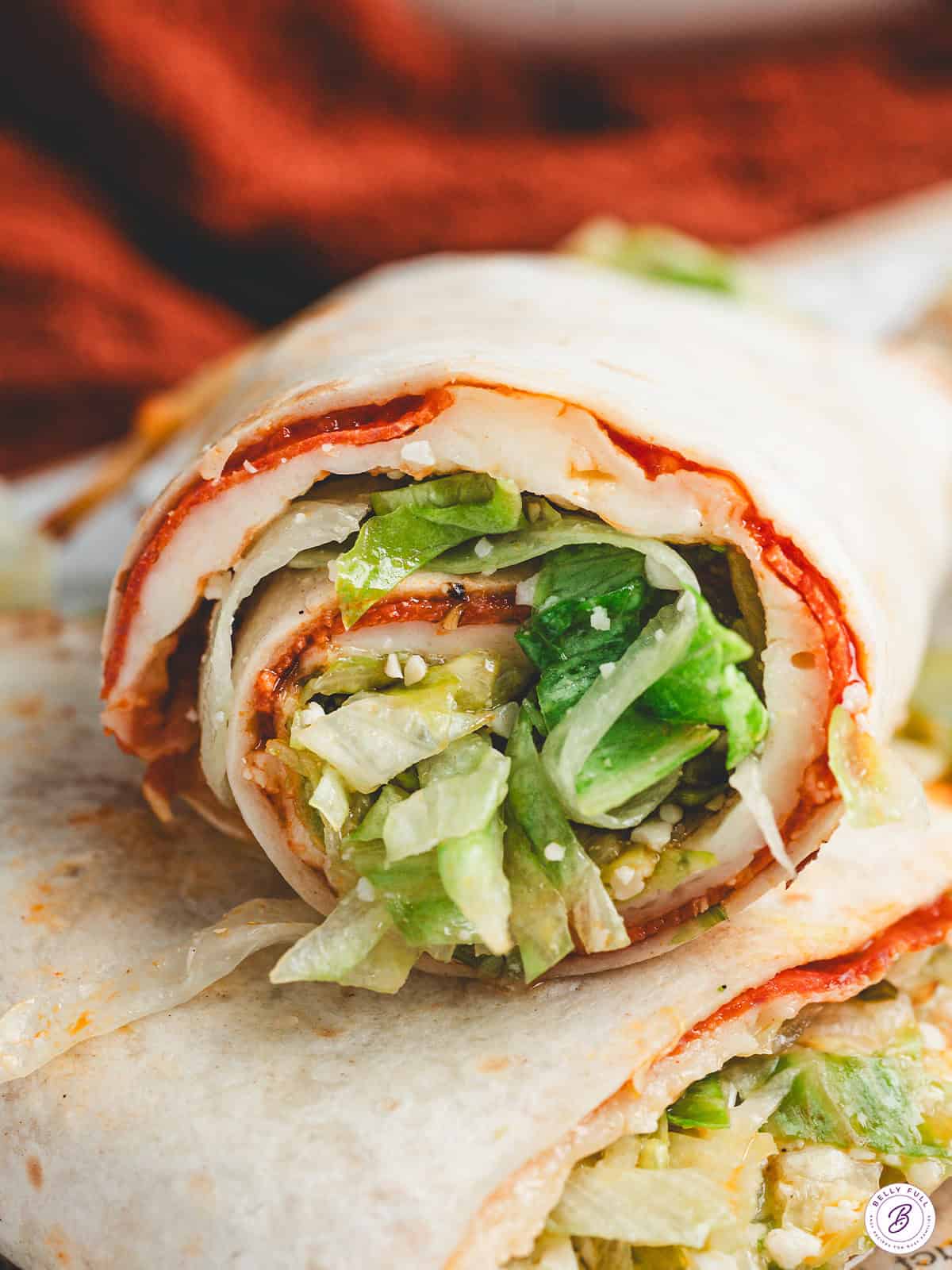 Rolled pizza salad wrap sliced to show layers of melted cheese, pepperoni, and lettuce filling.