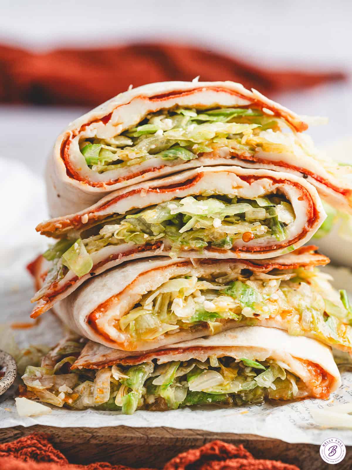 Stacked cheesy pizza salad wraps sliced open to show layers of melted cheese, pepperoni, and crisp lettuce.