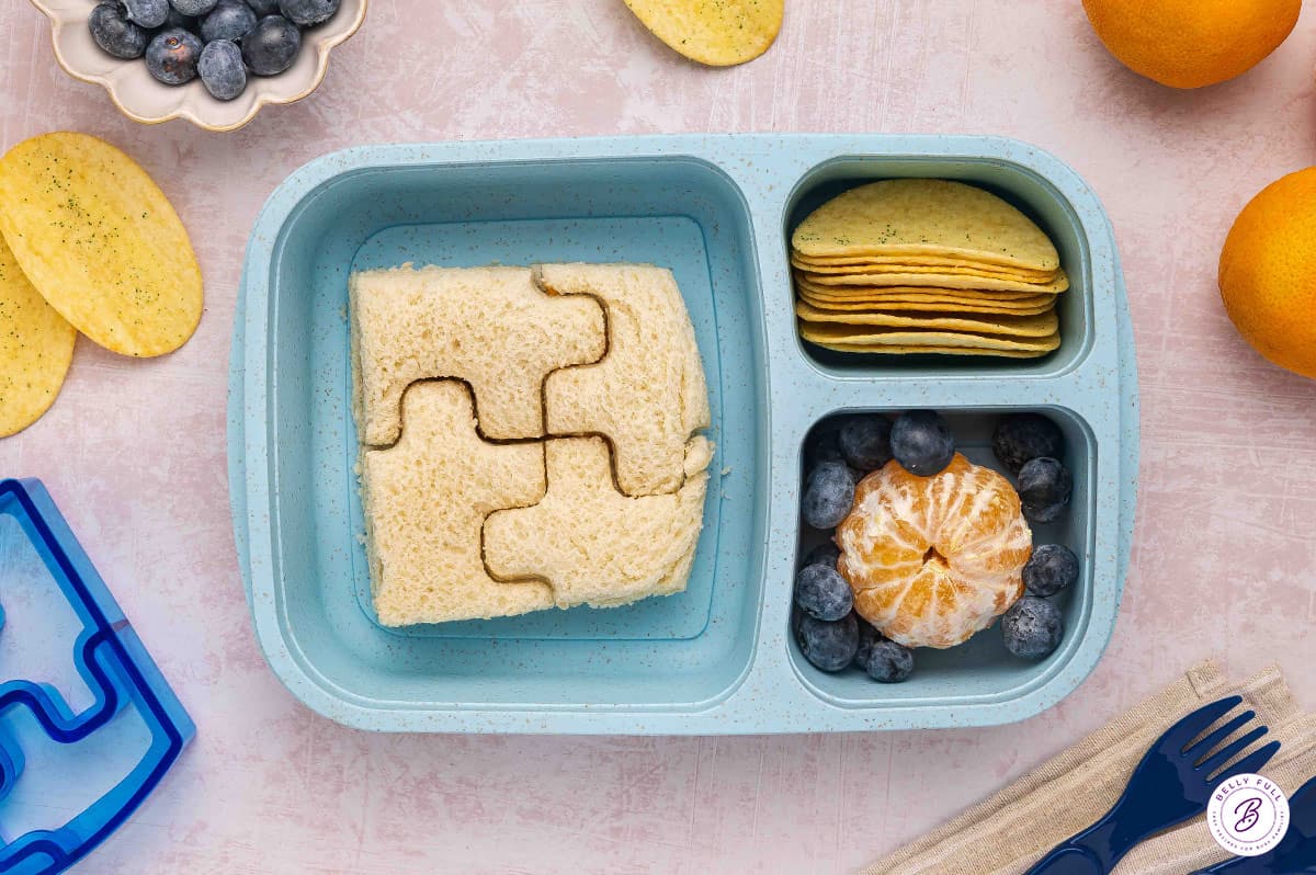 bento box for lunch with crustless sandwich, cut with a puzzle cookie cutter, chips, and fruit
