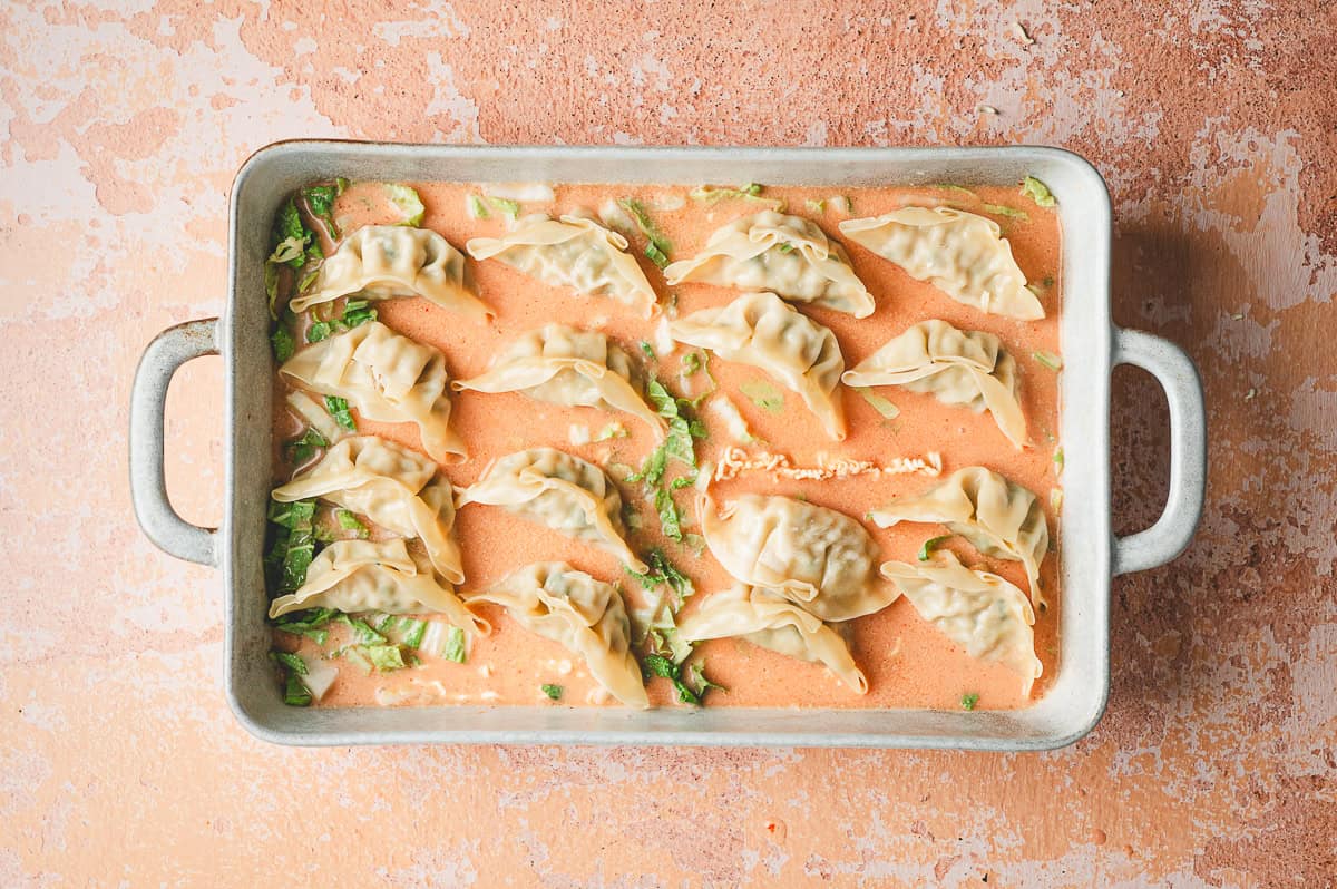 Unbaked casserole dish with frozen dumplings arranged in neat rows on top of the ramen and cabbage in the curry sauce.