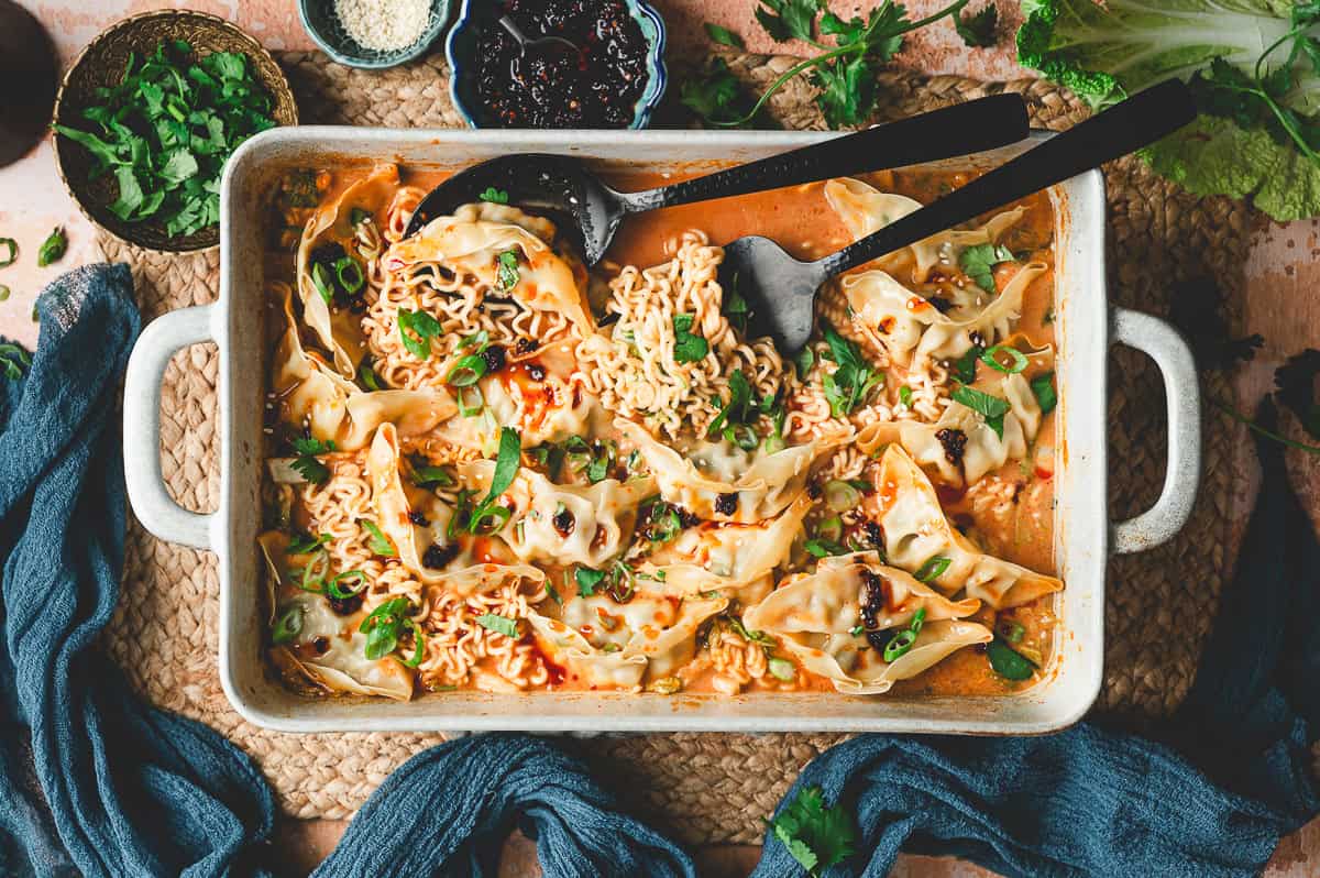 Overhead view of the finished Thai dumpling casserole with dumplings, ramen, and curry sauce, surrounded by small bowls of garnishes.