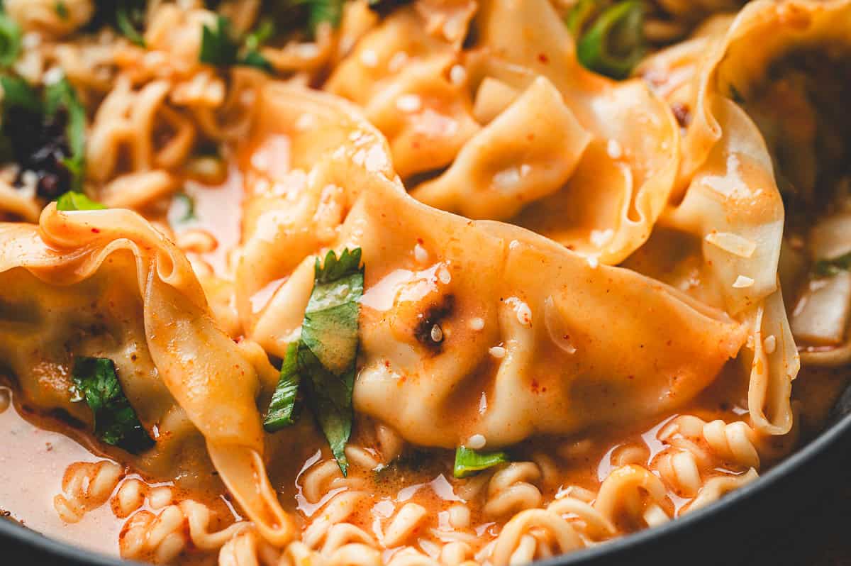 Close-up of a dumpling coated in curry sauce with ramen noodles and chopped cilantro, highlighting the texture and garnishes.