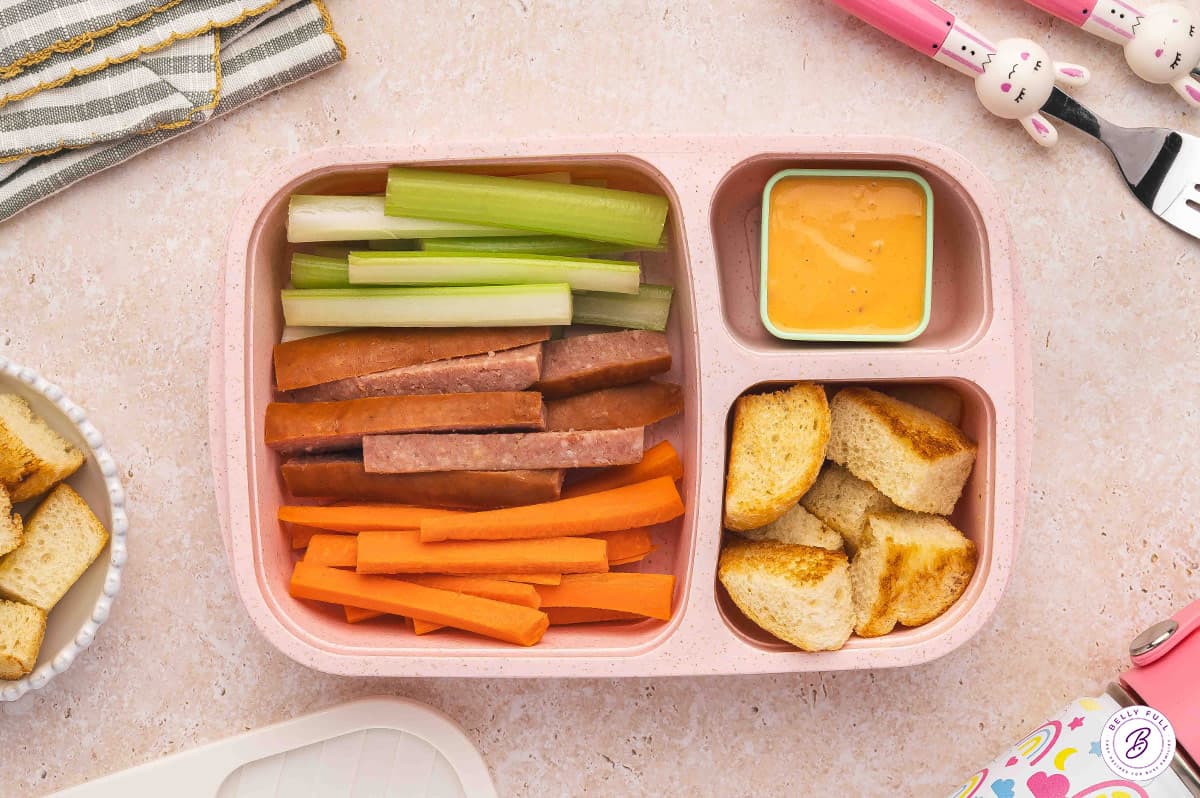 bento box for lunch with toasted bread cubes, celery, carrots, fully cooked kielbasa, with Thousand Island dressing