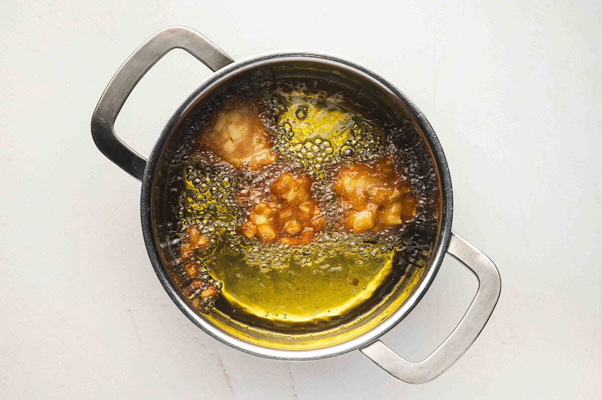 A pot of hot oil with several spoonfuls of apple fritter batter frying and bubbling.