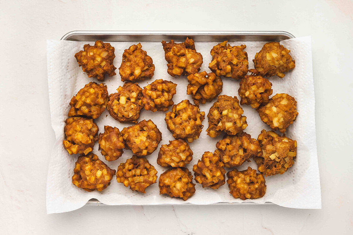 A tray lined with paper towels holding freshly fried apple fritters cooling.