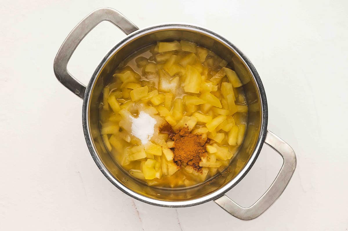 Cooked apples in a saucepan with added sugar and cinnamon on top before stirring.