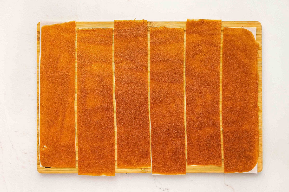 Apple fruit leather cut into long strips on a cutting board, ready to roll.