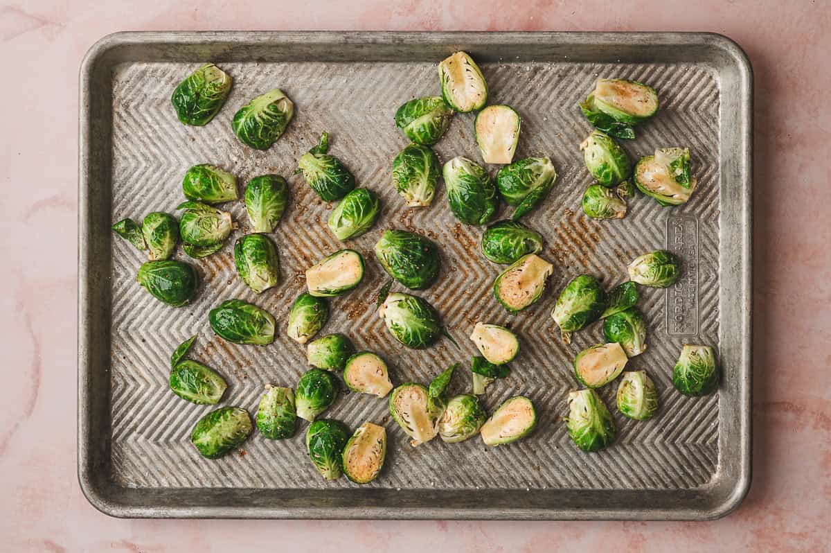 Seasoned brussels sprouts spread in a single layer on a baking sheet before roasting.
