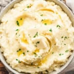 Bowl of creamy Boursin mashed potatoes topped with melting butter and sprinkled with fresh parsley.