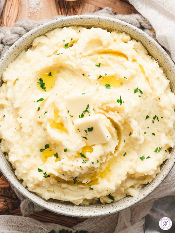 Bowl of creamy Boursin mashed potatoes topped with melting butter and sprinkled with fresh parsley.