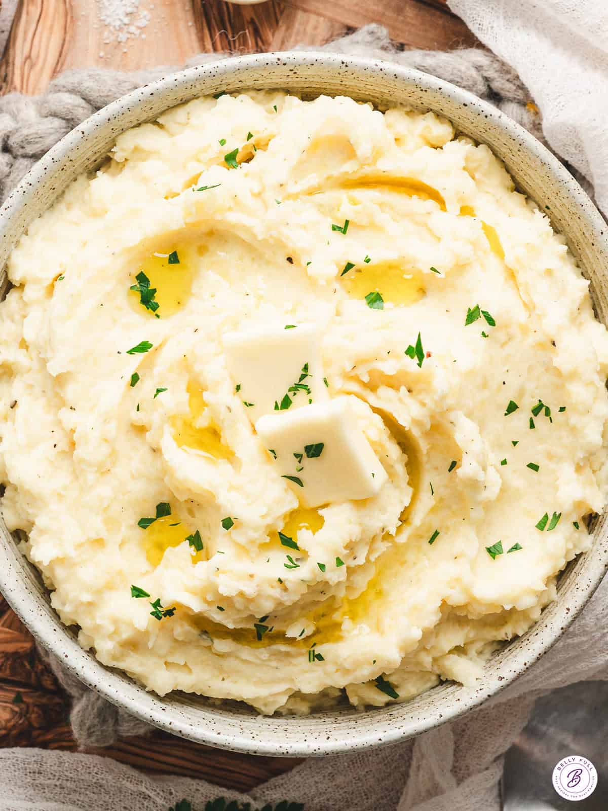 Bowl of creamy Boursin mashed potatoes topped with melting butter and sprinkled with fresh parsley.