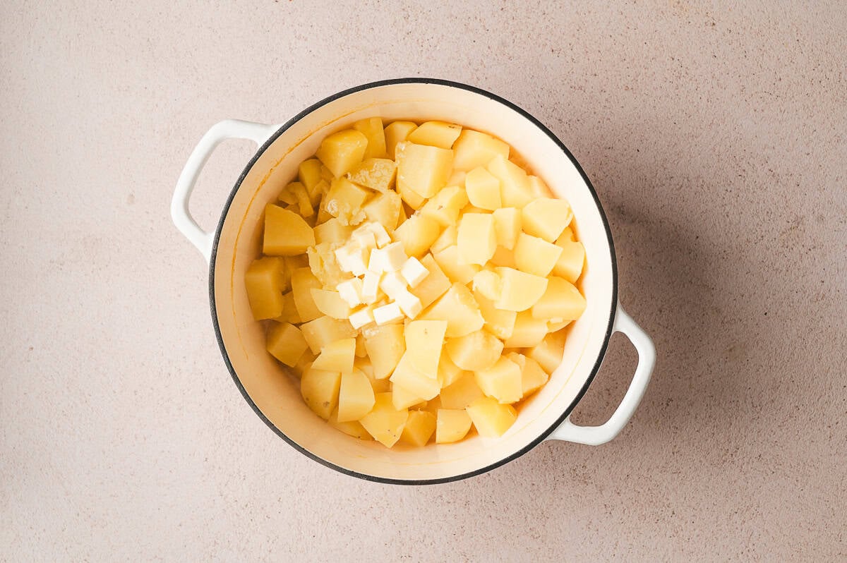 Cooked potato chunks drained and returned to the pot with diced butter on top.