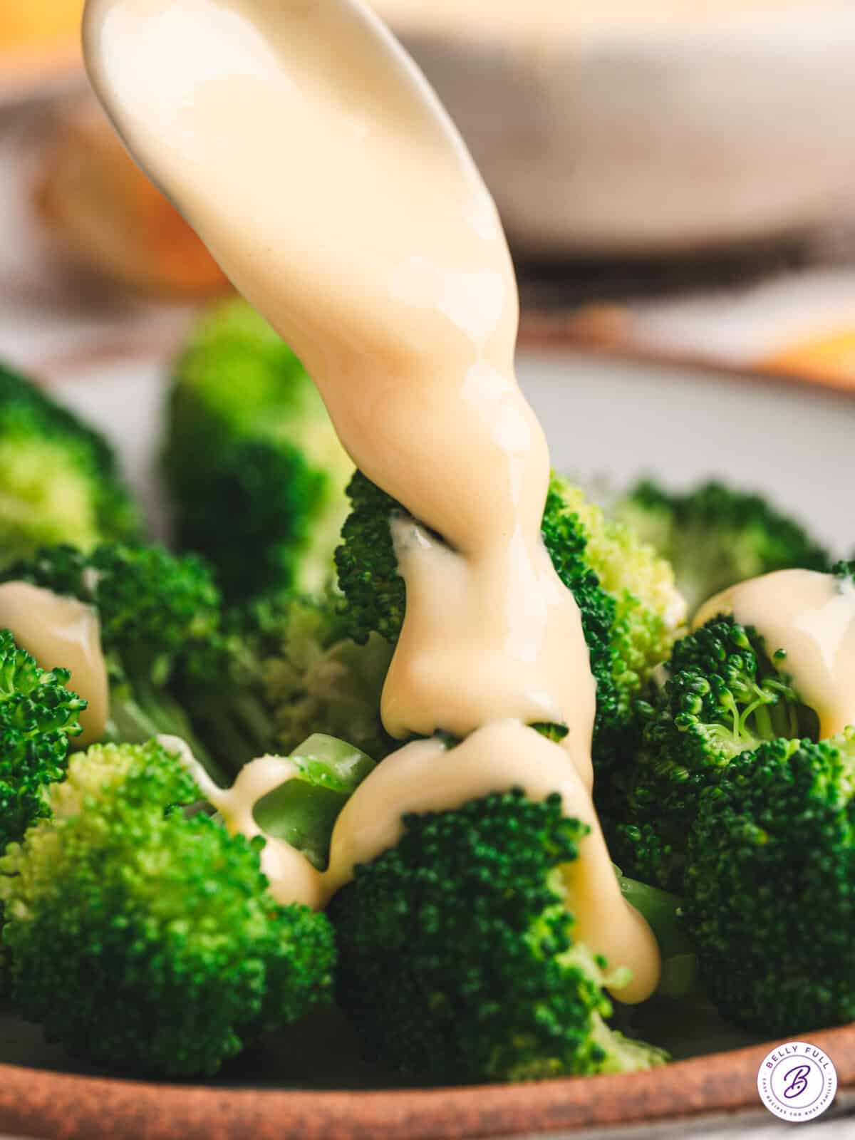 cheese sauce being poured over broccolie