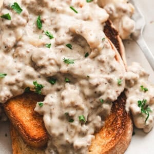 Close-up of creamed hamburger gravy with ground beef and onions spooned over golden toasted white bread, garnished with fresh parsley.