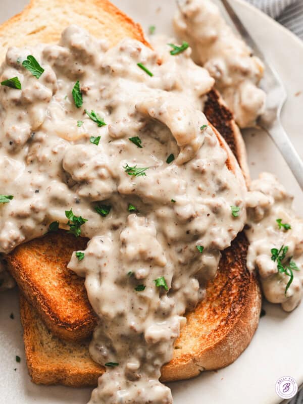 Close-up of creamed hamburger gravy with ground beef and onions spooned over golden toasted white bread, garnished with fresh parsley.