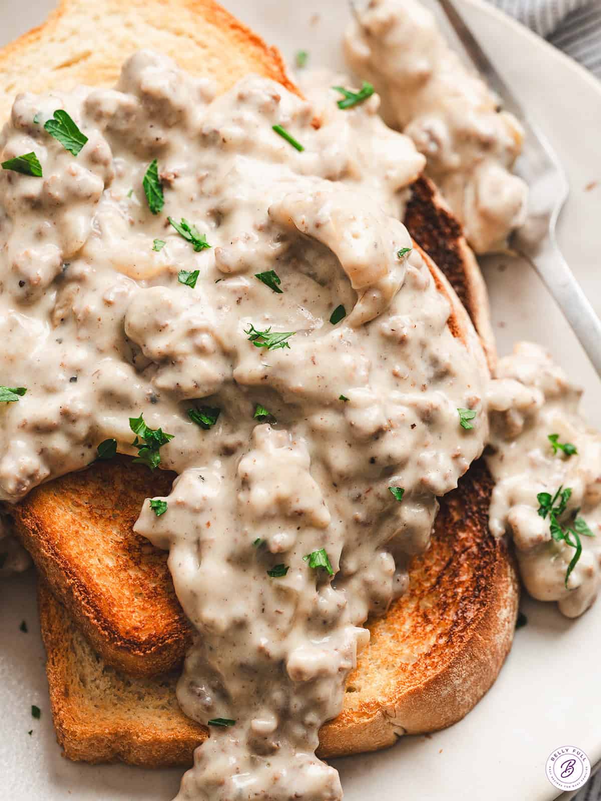 Close-up of creamed hamburger gravy with ground beef and onions spooned over golden toasted white bread, garnished with fresh parsley.