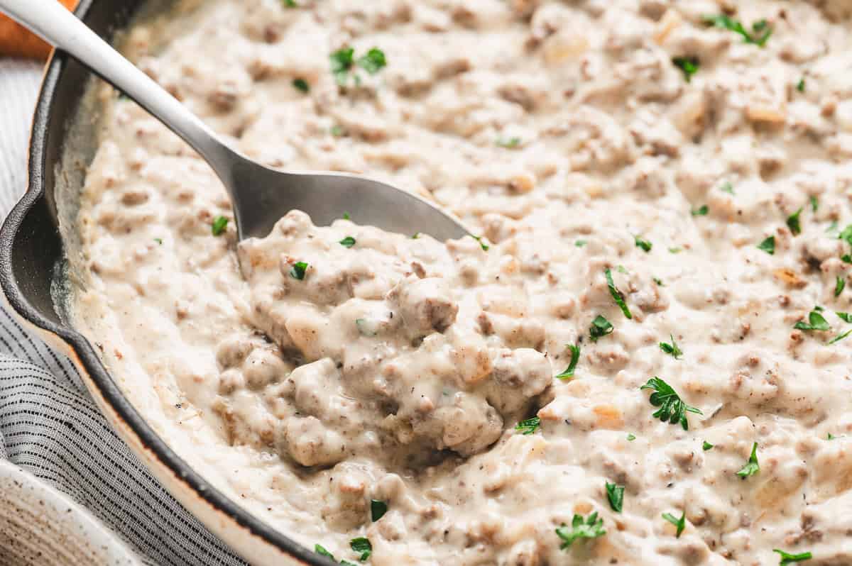 Creamed hamburger gravy thickened and simmered in a skillet, garnished with fresh parsley.