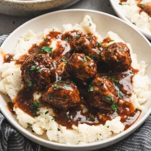Bowl of Salisbury steak meatballs served over mashed potatoes, topped with rich brown gravy and fresh parsley.