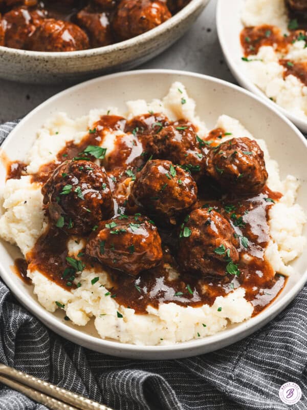 Bowl of Salisbury steak meatballs served over mashed potatoes, topped with rich brown gravy and fresh parsley.