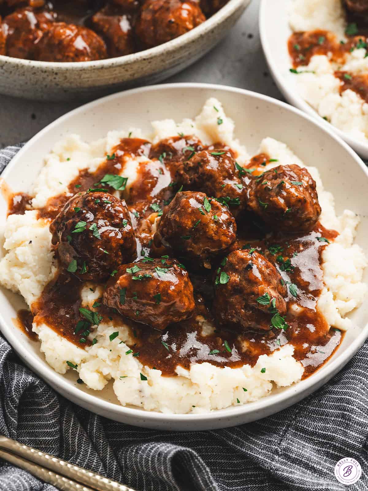 Bowl of Salisbury steak meatballs served over mashed potatoes, topped with rich brown gravy and fresh parsley.