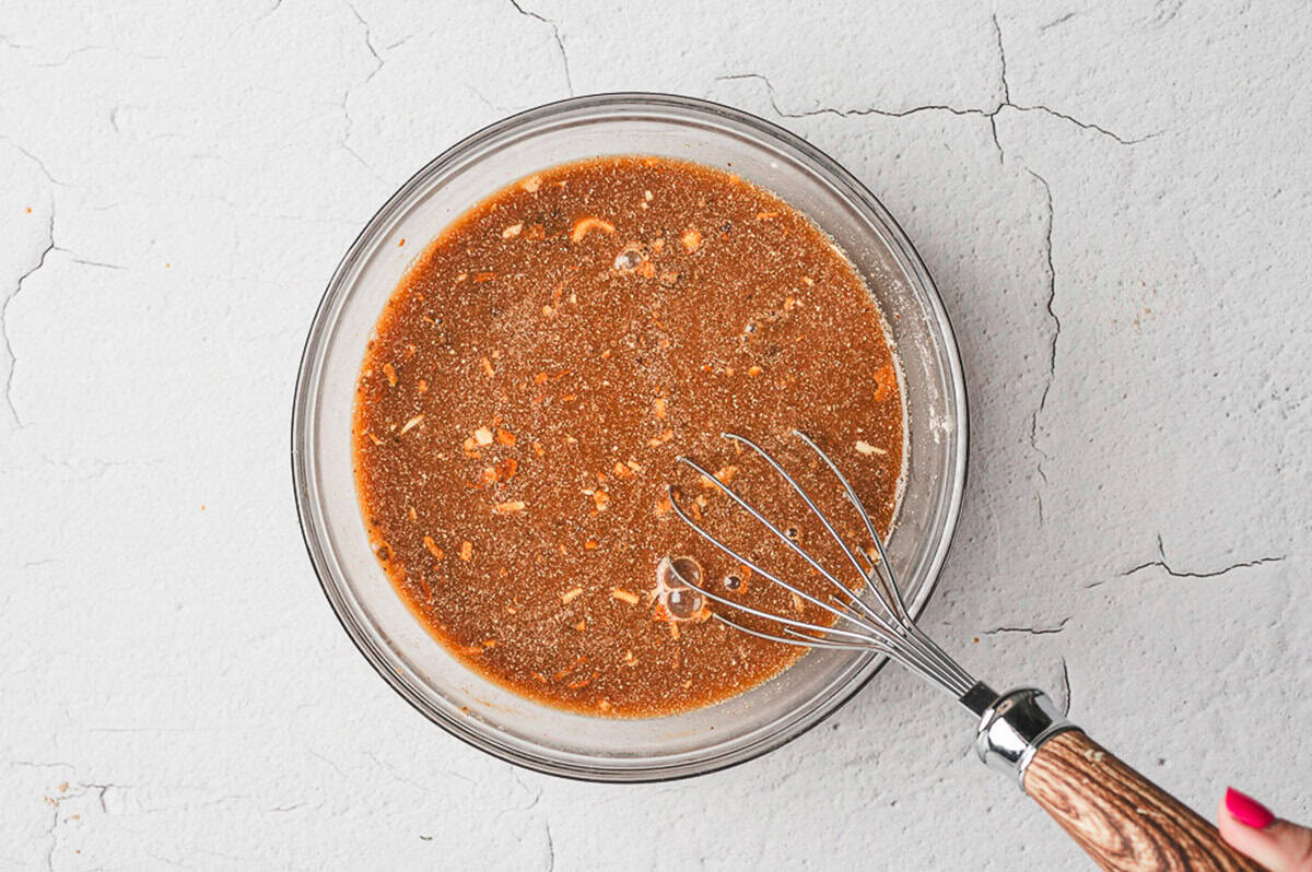 Glass bowl filled with brown gravy mixture and a whisk on the side.