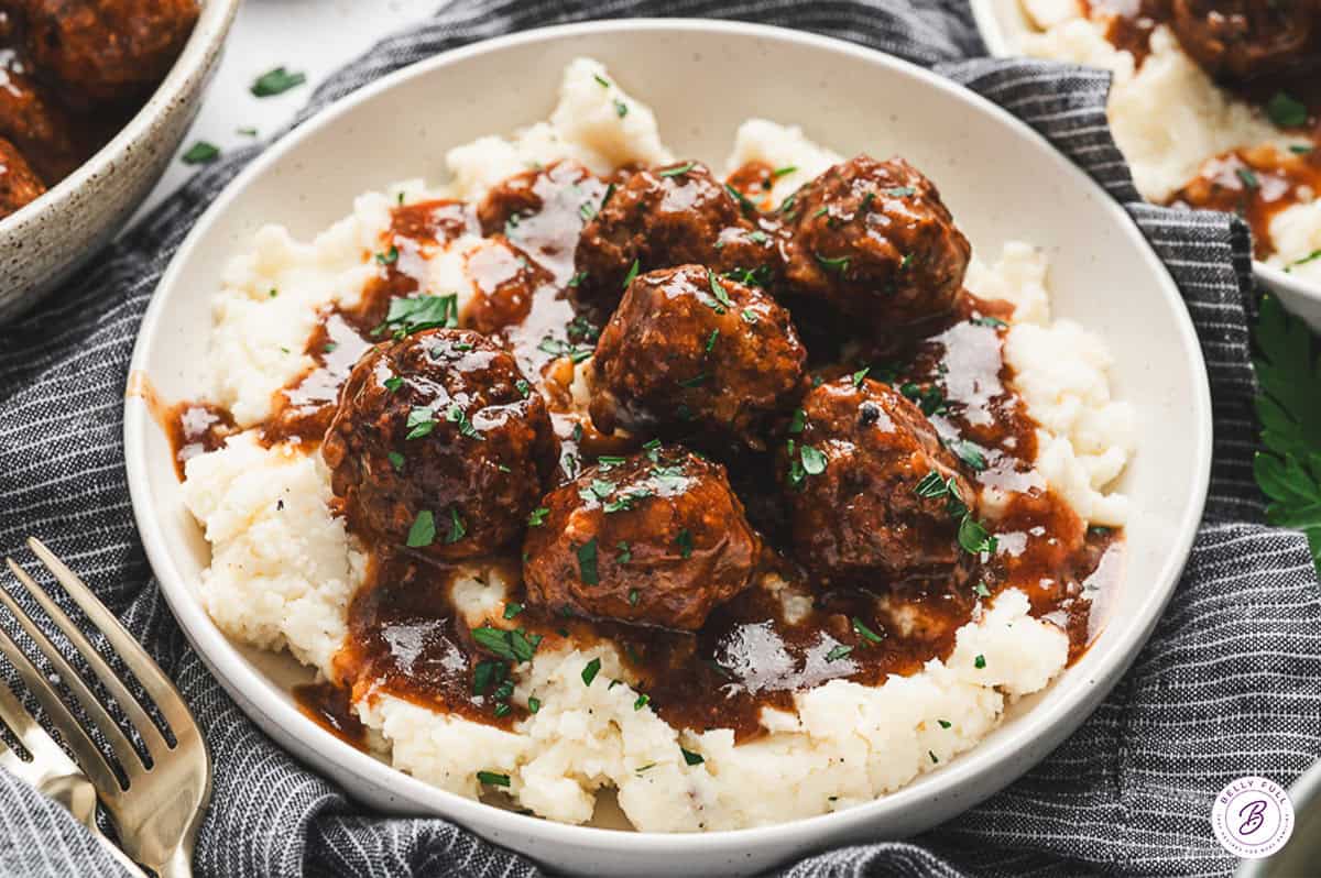 Plate of Salisbury steak meatballs over mashed potatoes, topped with gravy and parsley.