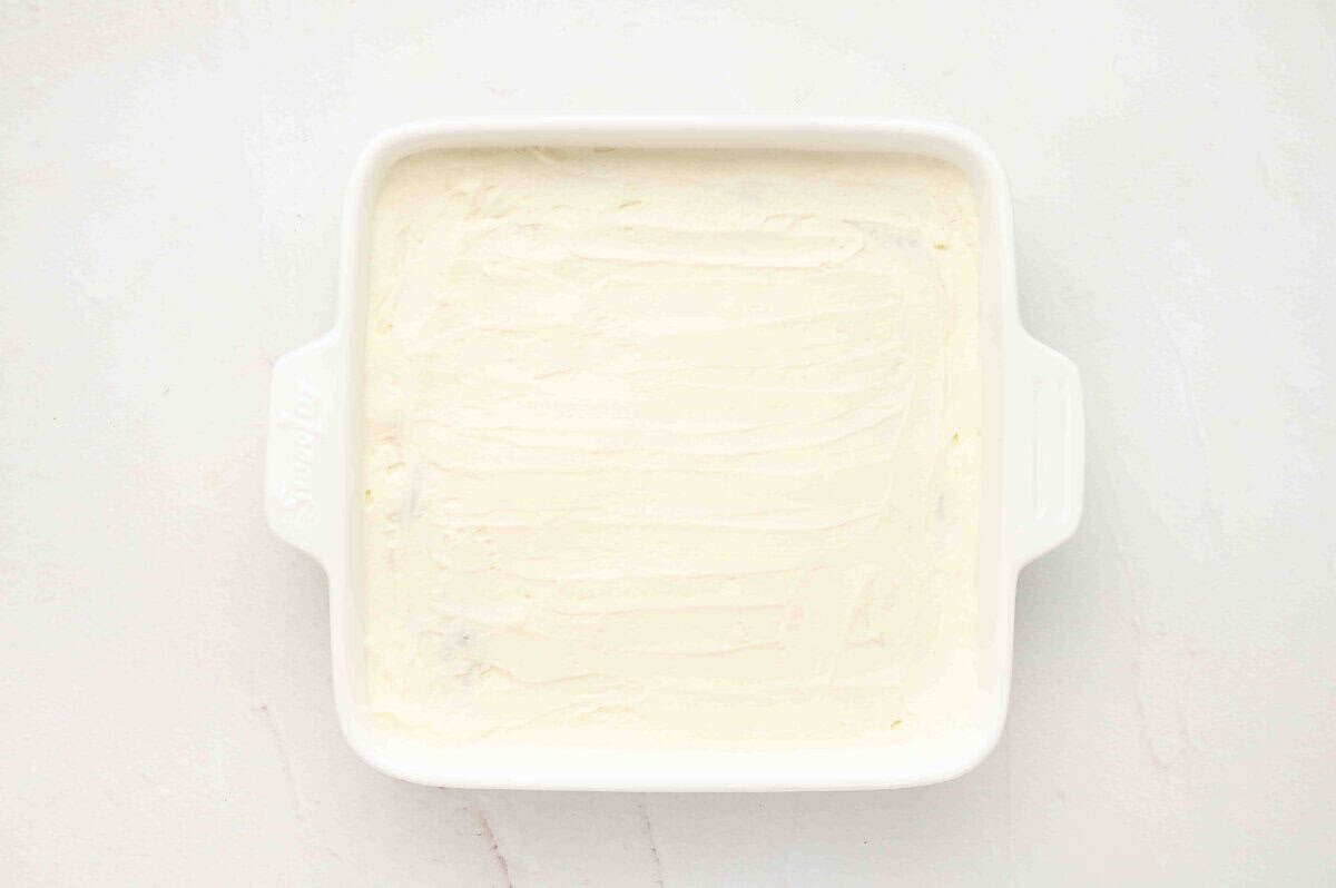 The baking dish with cream spread smoothly over the top layer of Oreos, forming the final layer.