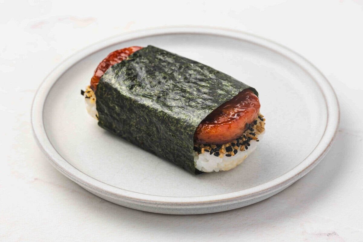 Finished Spam Musubi on a plate wrapped in a strip of nori with furikake showing between rice and spam