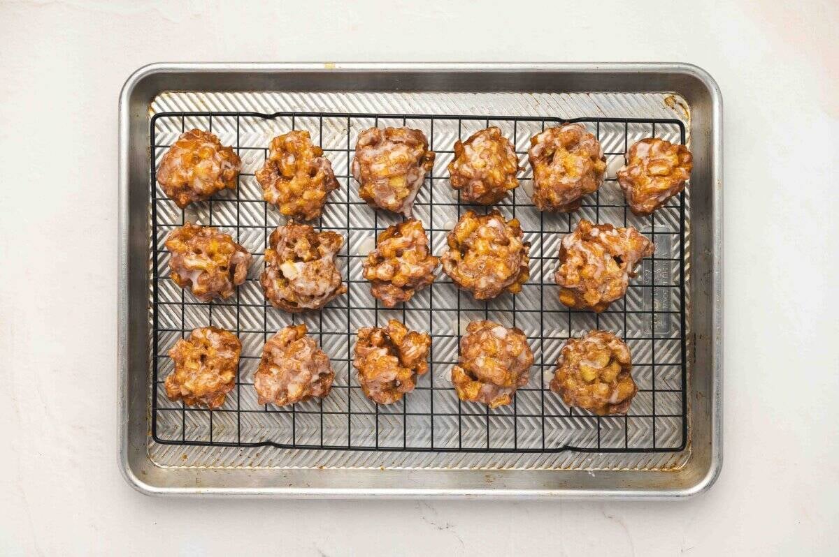 Freshly glazed apple fritters cooling on a wire rack set over a baking sheet.