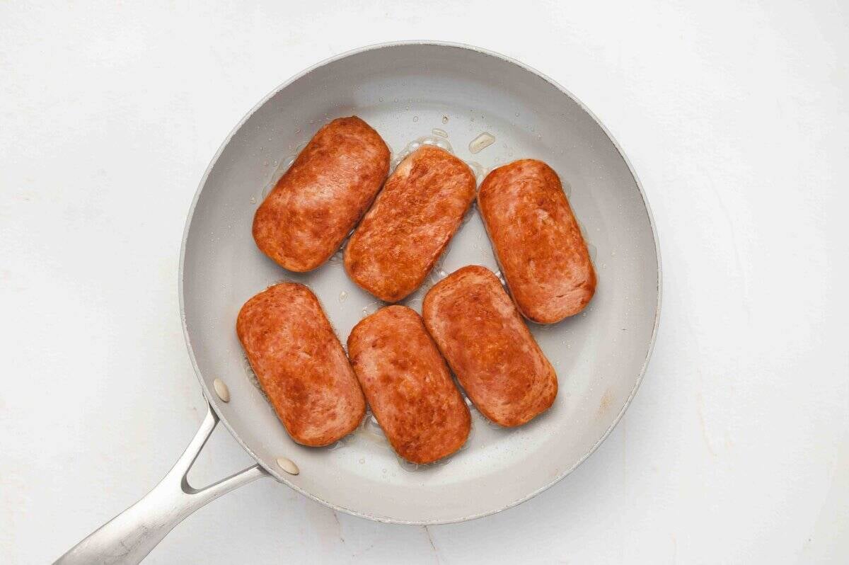 Six slices of Spam frying in a nonstick skillet until golden brown