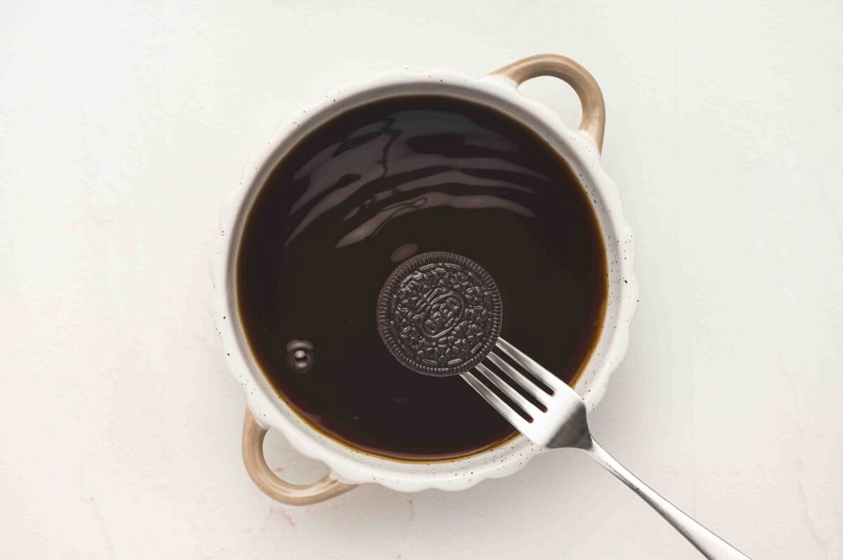 An Oreo cookie being dipped into the coffee mixture using a fork.