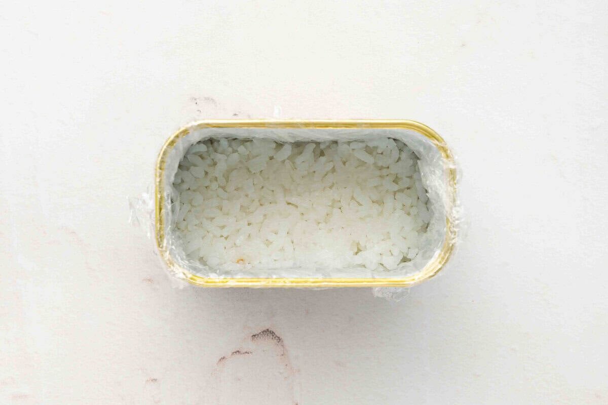 Empty Spam can lined with plastic wrap and filled with pressed sushi rice