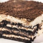 A close-up slice of Oreo tiramisu showing distinct layers of coffee-soaked Oreos and fluffy mascarpone cream, topped with crushed Oreo crumbs.