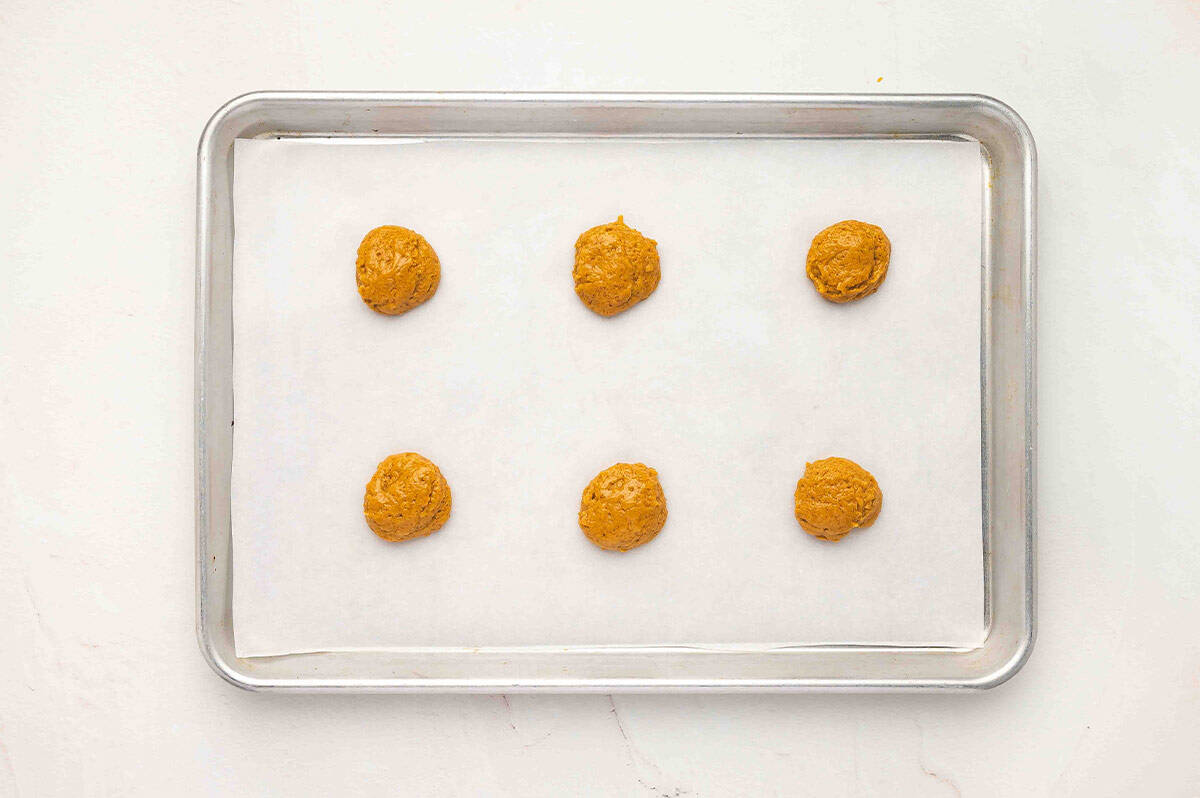 A baking sheet lined with parchment paper with six spoonfuls of pumpkin batter evenly spaced apart.